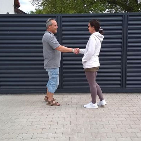 Dvě osoby se podávají ruce před posuvnou garážovou branou, což symbolizuje spokojenost a důvěru v produkty a služby VRATA-L&V.
